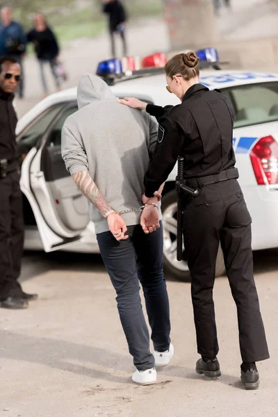 Vista trasera de la mujer policía con delincuente detenido esposado - foto de stock