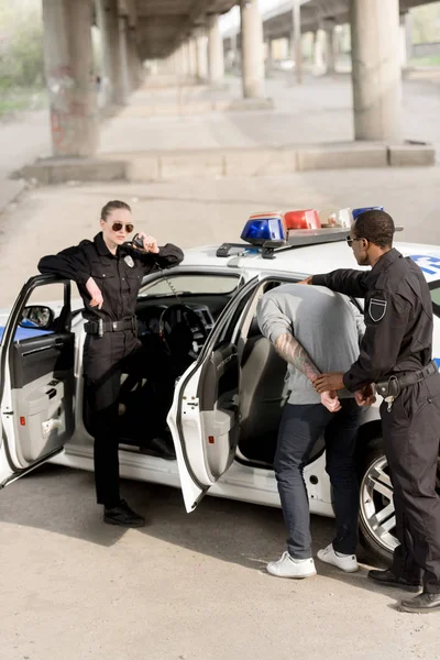 Policewoman talking on portable radio while her partner holding criminal — Stock Photo