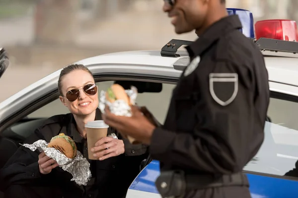 Cropped shot of african american policeman having lunch with policewoman holding coffee cup — Stock Photo