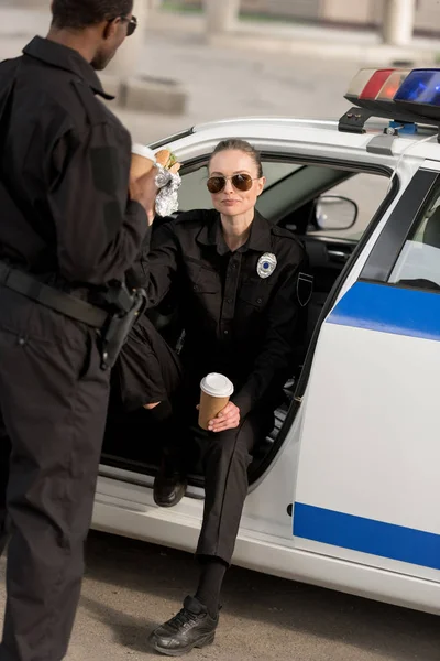 Mujer policía en gafas de sol almorzando con pareja afroamericana - foto de stock