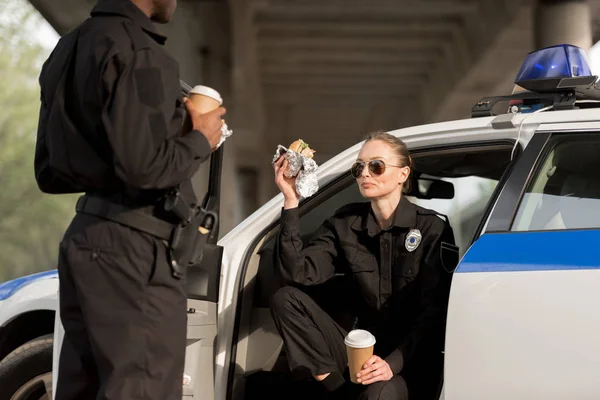 Two police officers drinking coffee and eating burger — Stock Photo