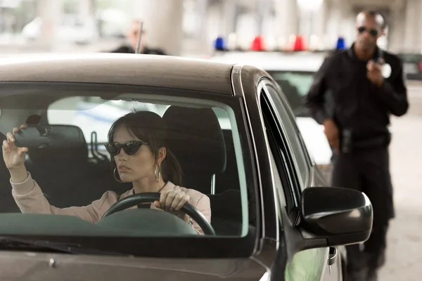 African american policeman approaching to car of young woman in sunglasses — Stock Photo