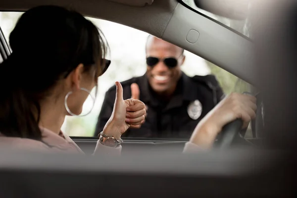 Young female driver in car and smiling policeman doing thumb up gesture to each other — Stock Photo