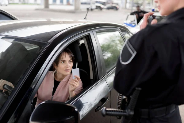 Policewoman with portable radio and young woman in car holding driver license — Stock Photo