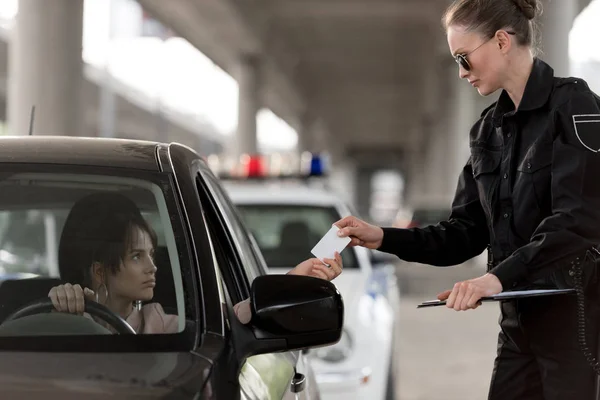 Jovem mulher no carro dando carteira de motorista para policial em óculos de sol — Fotografia de Stock