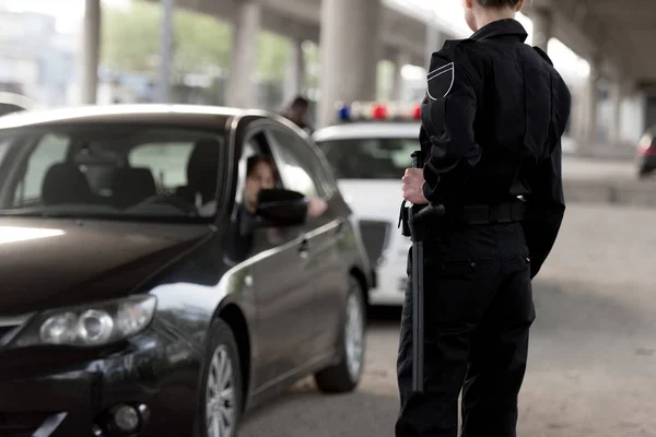 Cropped shot of policewoman holding truncheon and stopped car — Stock Photo