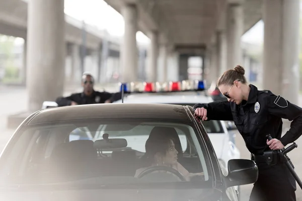 Policewoman in sunglasses talking to woman sitting in car and policeman standing behind near car — Stock Photo