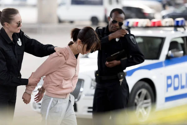 Policial segurando preso jovem mulher enquanto seu parceiro falando no rádio portátil — Fotografia de Stock