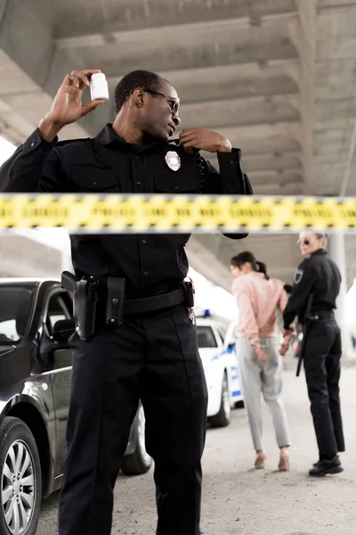 Policía afroamericano sosteniendo píldoras frasco con drogas y hablando en la radio portátil - foto de stock