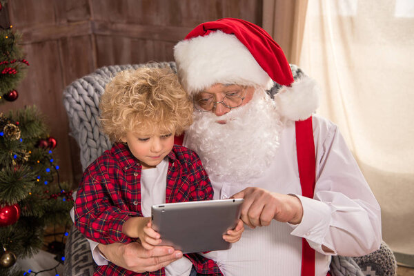 Santa Claus with kid on knee using tablet