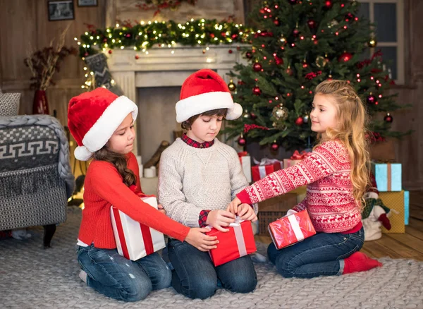Crianças em chapéus de Santa com caixas de presente — Fotografia de Stock