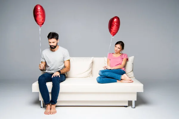 Couple sitting on couch with red balloons — Stock Photo, Image