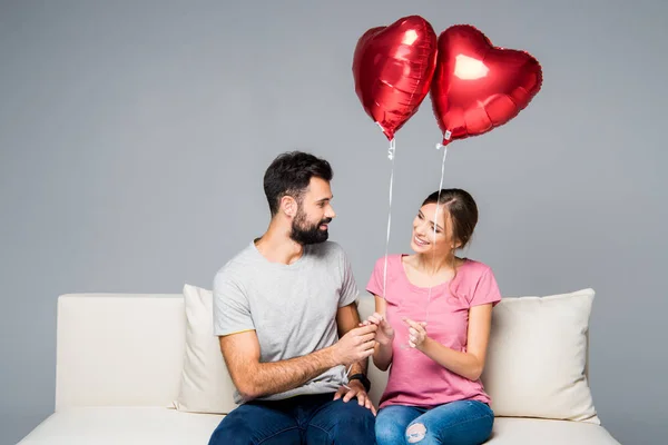 Pareja sentada en sofá con globos rojos —  Fotos de Stock