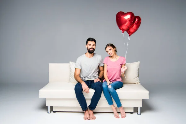 Pareja sentada en sofá con globos rojos —  Fotos de Stock