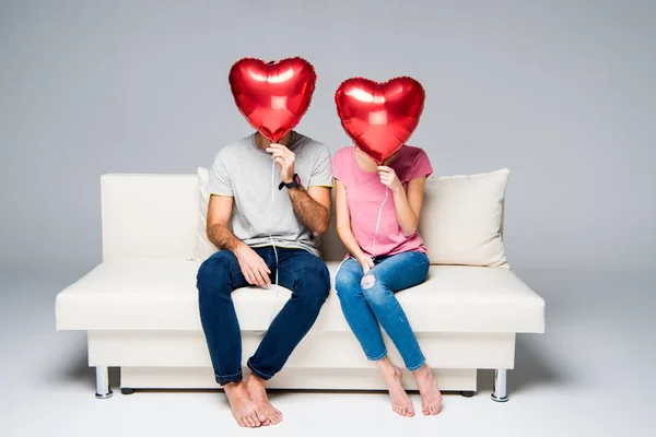 Casal sentado no sofá com balões vermelhos — Fotografia de Stock