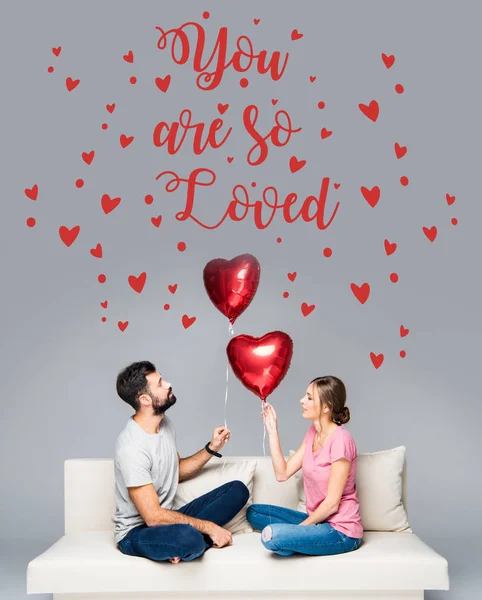 Couple sitting on couch with red balloons Royalty Free Stock Images