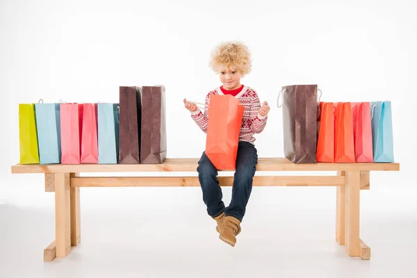 Niño con bolsas de compras sentado en el banco - foto de stock