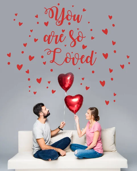 Pareja sentada en sofá con globos rojos - foto de stock