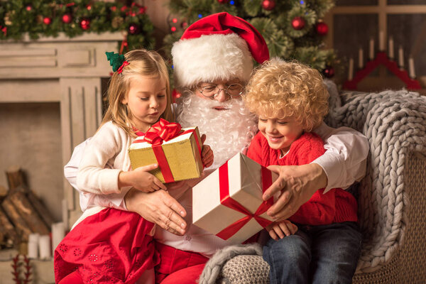 Санта-Клаус с детьми, держащими подарочные коробки
  