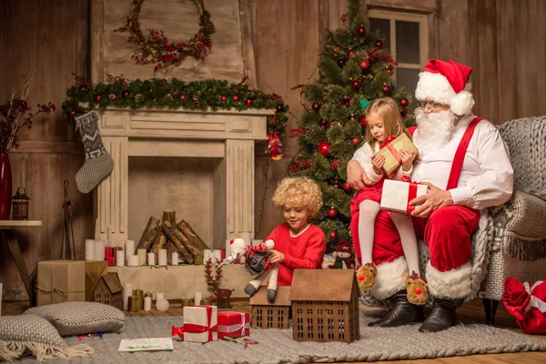 Papai Noel e crianças sentadas perto da lareira — Fotografia de Stock