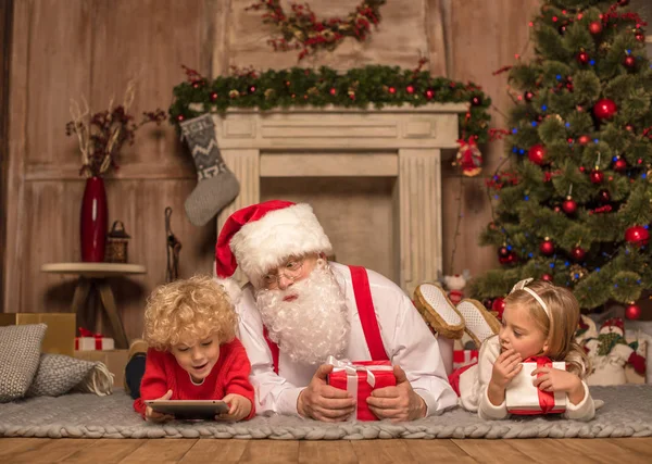 Kerstman en kinderen liggen op tapijt — Stockfoto