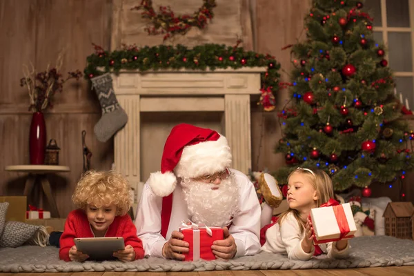Kerstman en kinderen liggen op tapijt — Stockfoto