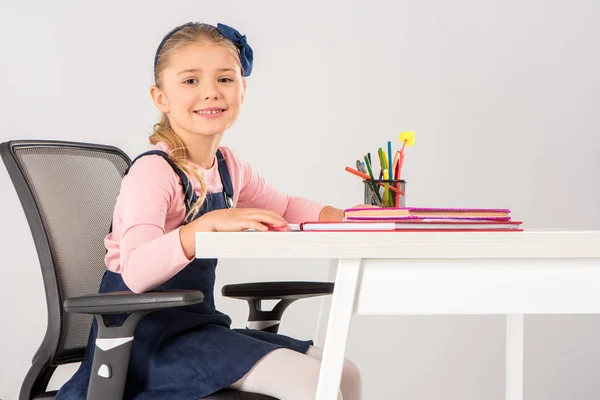 Colegiala sonriente sentada en el escritorio con libros — Foto de Stock