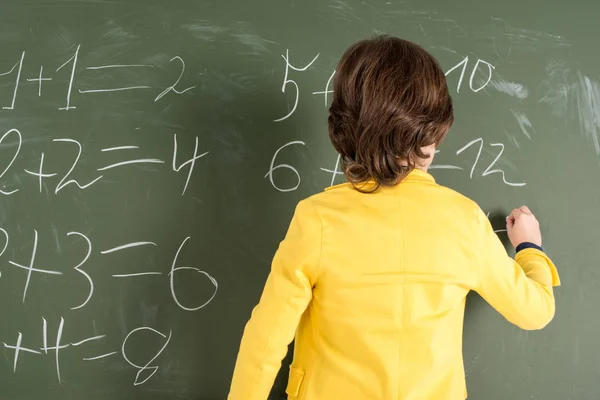Schoolboy writing on blackboard — Stock Photo