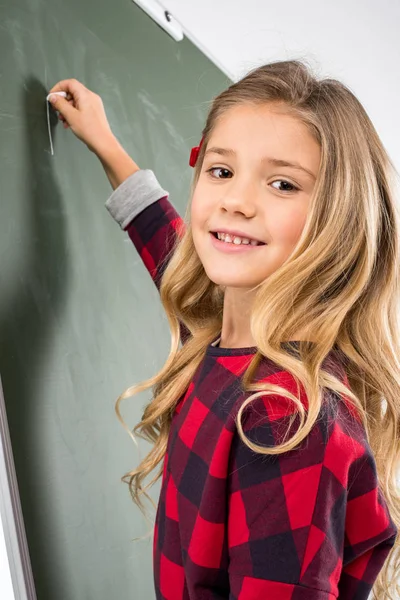 Schoolgirl writing on blackboard — Stock Photo