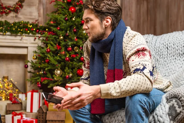 Человек в трикотажном свитере держит смартфон — стоковое фото