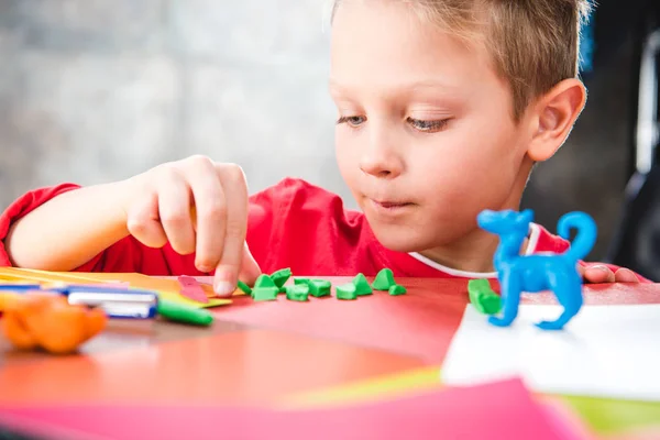 Schoolchild making toy from plasticine — Stock Photo, Image