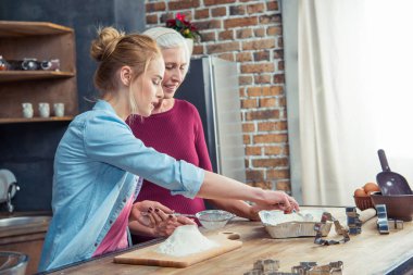 Grandmother and granddaughter sifting flour clipart