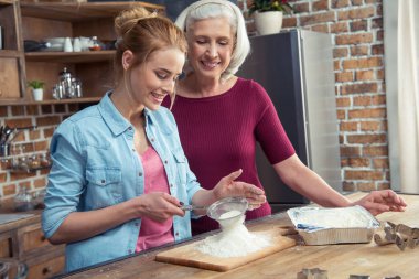 Grandmother and granddaughter sifting flour clipart
