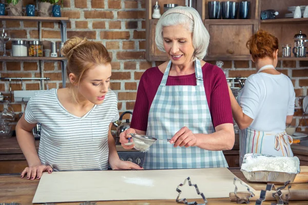 Grandmother and granddaughter sifting flour — Stock Photo, Image