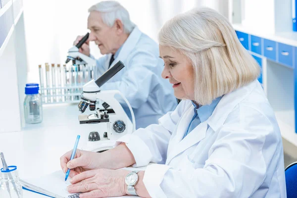 Químicos senior escribiendo en bloc de notas — Foto de Stock