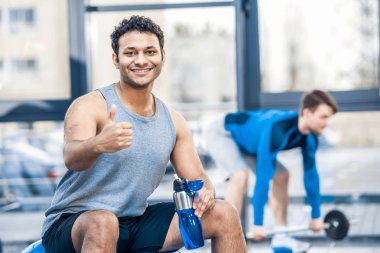man with bottle of water resting at gym clipart