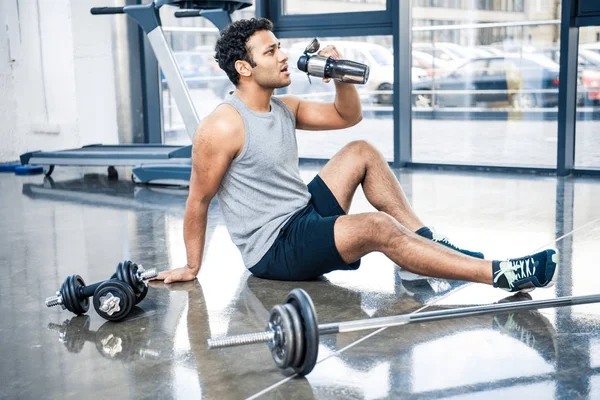 Hombre con botella de agua descansando en el gimnasio — Foto de Stock