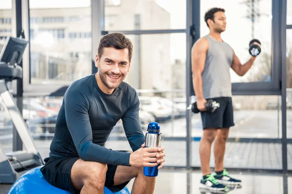 Чоловік з пляшкою води відпочиває в спортзалі — стокове фото