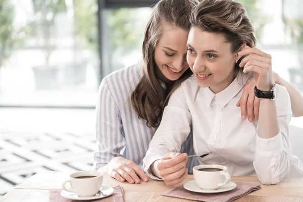 Lachende vriendinnen koffie drinken en omarmen — Stockfoto