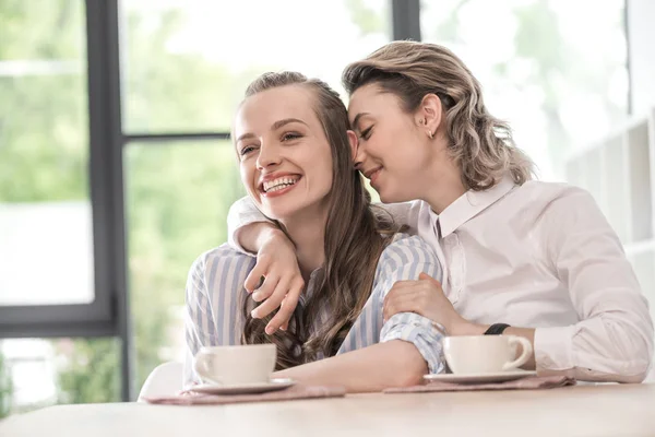 Sorrindo namoradas bebendo café e abraçando — Fotografia de Stock