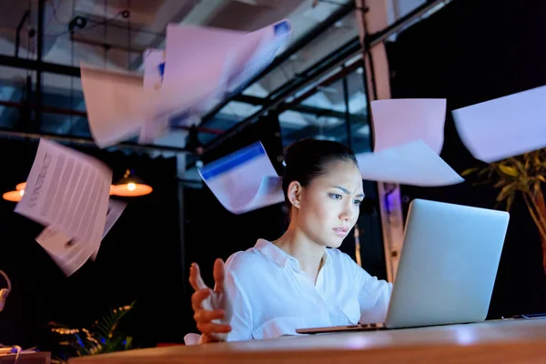 Деловая женщина работает на ноутбуке и бросает документы — стоковое фото