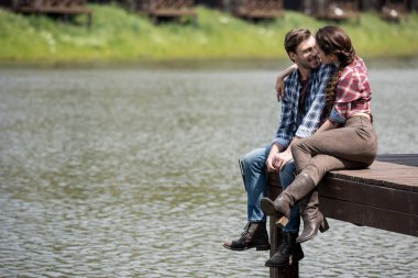 young couple sitting on wooden pier clipart