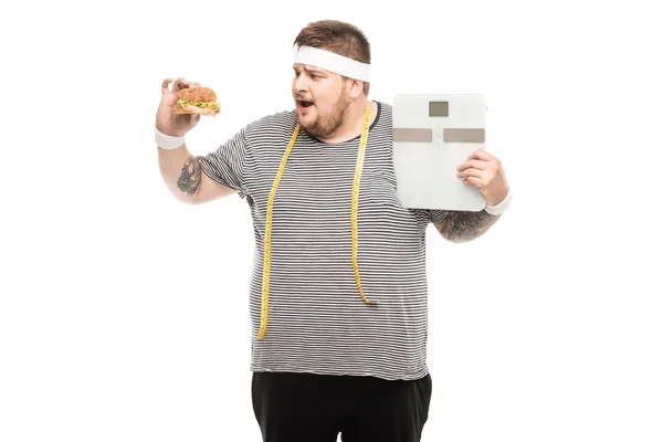 Homem segurando escalas do corpo e hambúrguer — Fotografia de Stock