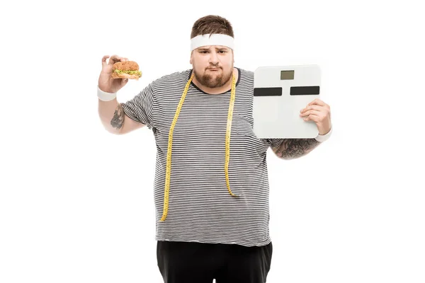 Man holding body scales and burger — Stock Photo, Image