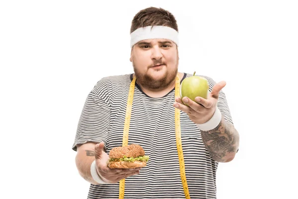 Gordita hombre sosteniendo hamburguesa y manzana — Foto de Stock