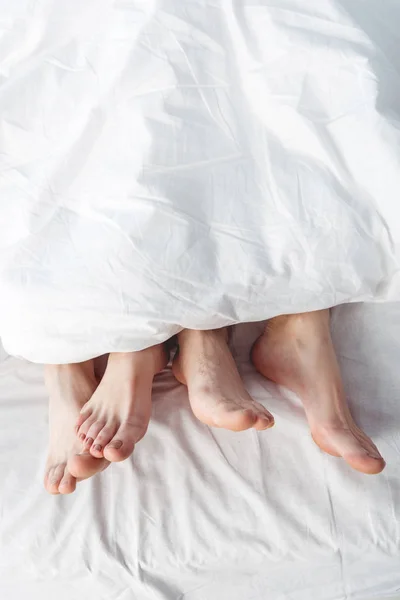 Pies de pareja acostada en la cama — Foto de Stock