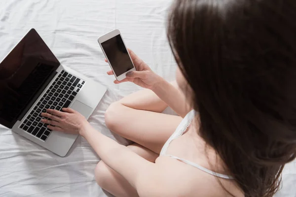 Жінка зі смартфоном за допомогою ноутбука — стокове фото