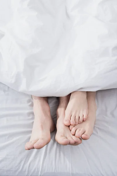Pés de casal que se estende fora de cobertor — Fotografia de Stock