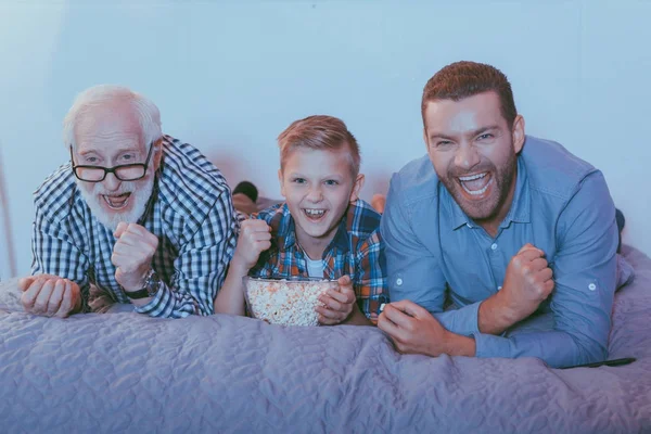 Família rindo com pipocas na cama — Fotografia de Stock