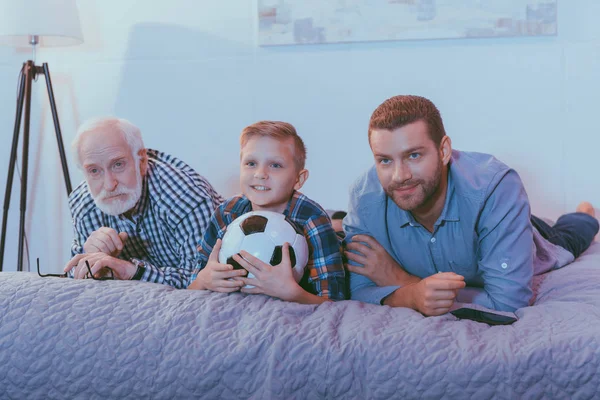 Familj titta på fotboll på säng — Stockfoto